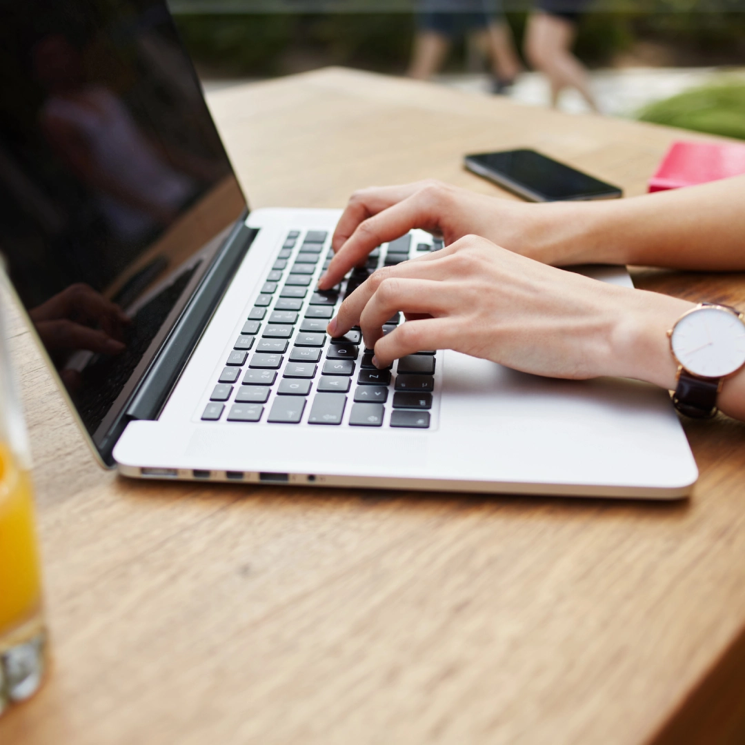 Hands typing on a laptop at a wooden table.