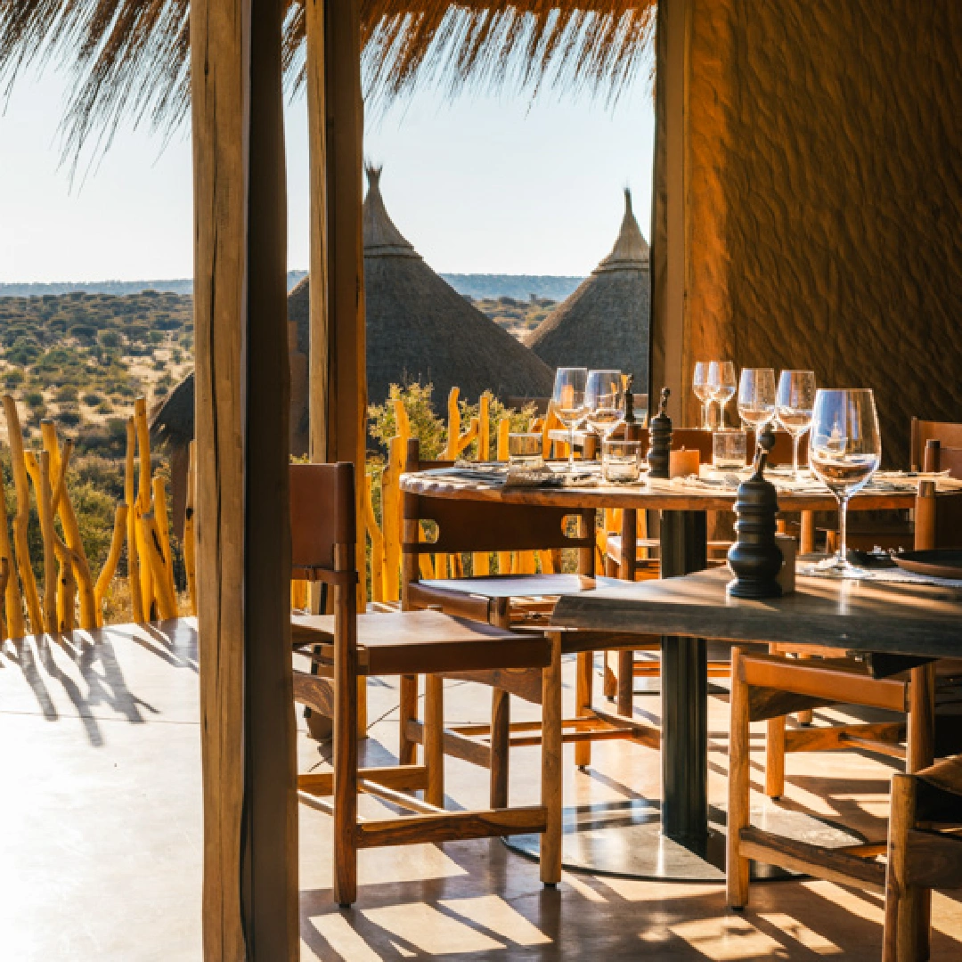 Outdoor dining tables set with wine glasses overlooking a savanna landscape.