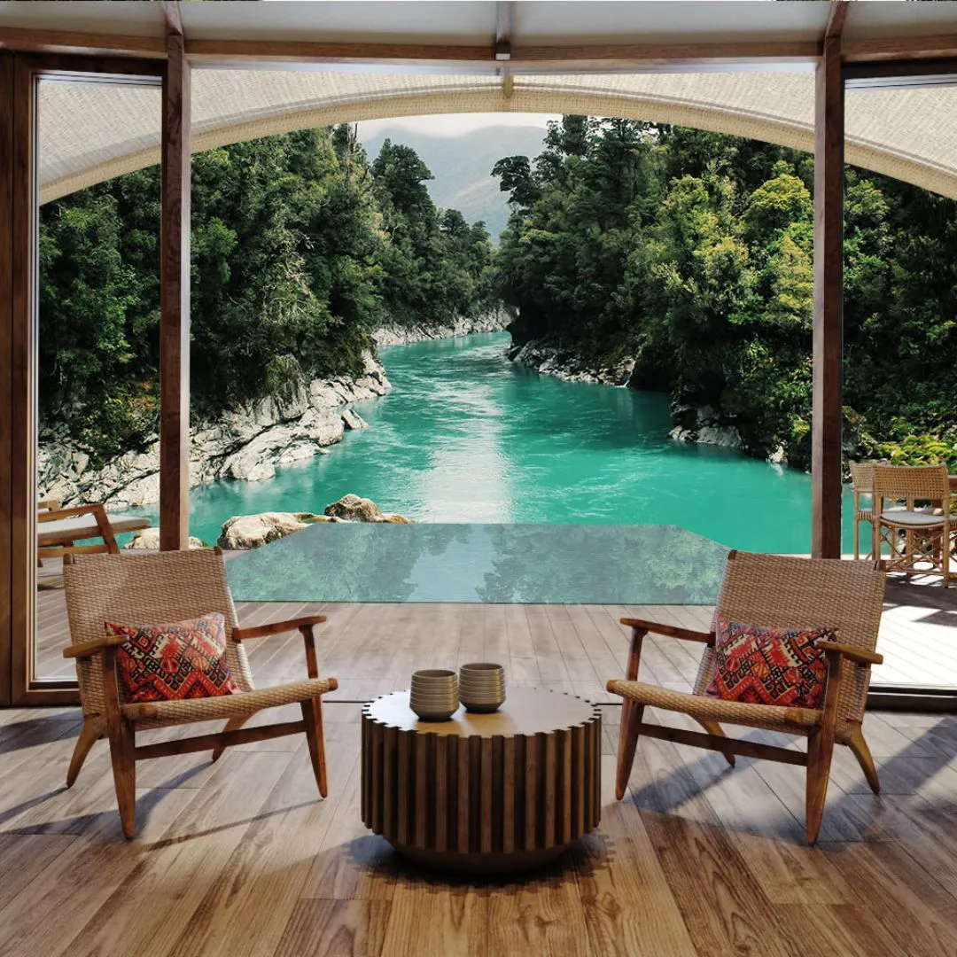 A luxury indoor sitting area with woven armchairs looking out past an infinity pool toward a vibrant turquoise river flowing through a lush, forested canyon.